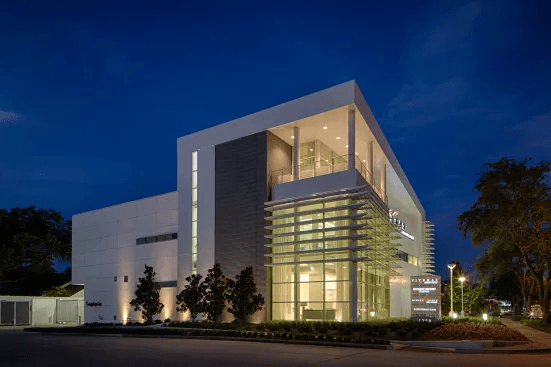 Exterior of 4208 Richmond at dusk, showing its glass entrance and three-story architectural massing, with no people visible.